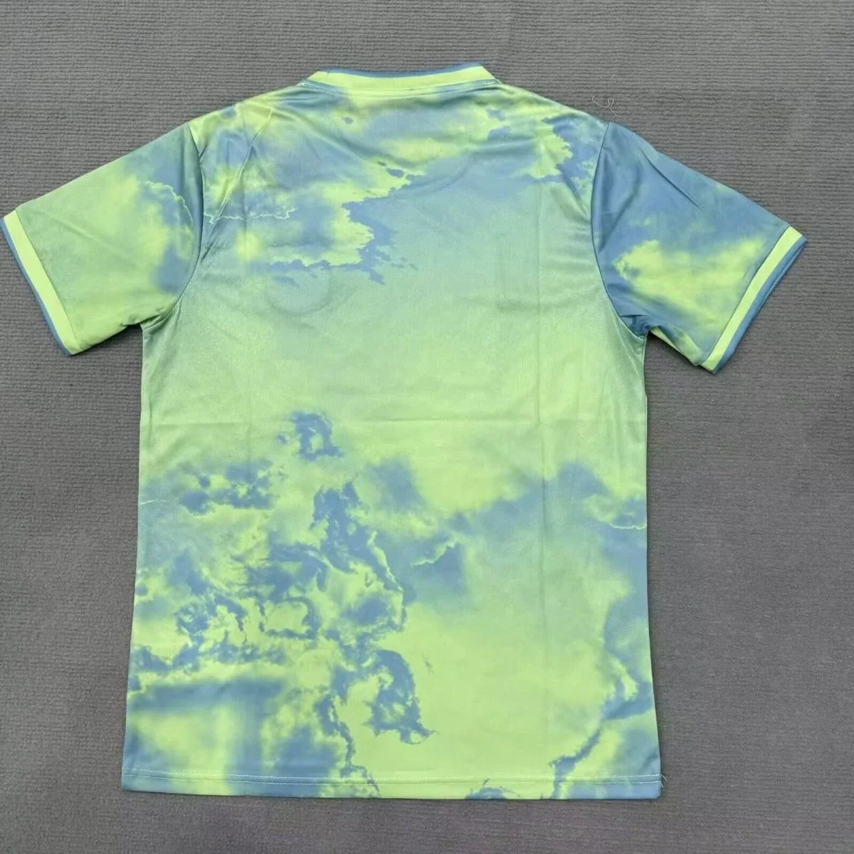 Back view of the lime green Barcelona shirt with gray-blue cloudlike patterns across the shoulders, sleeves and lower back, laid flat on gray fabric.