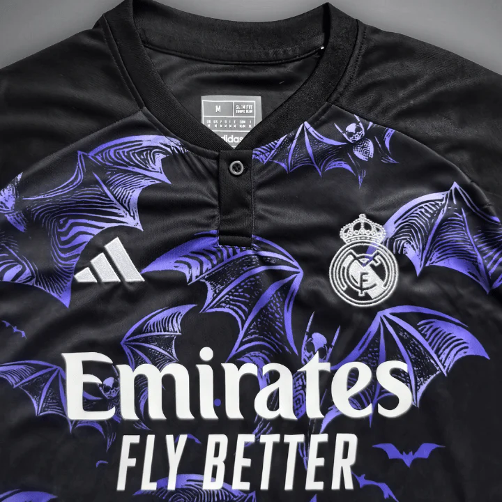 Chest close-up of the Real Madrid Bats Attack shirt, with a black button neckline, purple bat illustrations, white crest and adidas mark, and Emirates Fly Better lettering