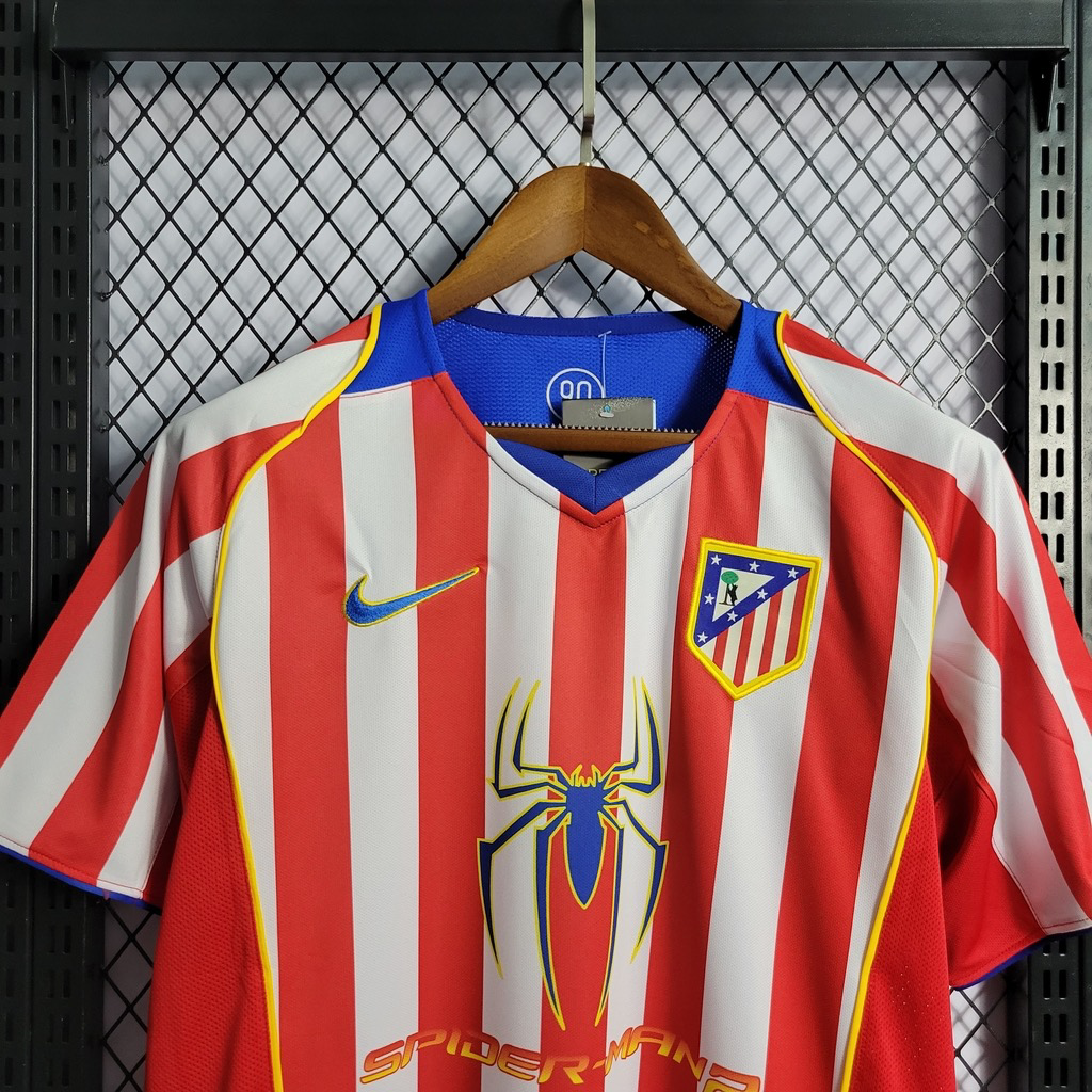 Upper-front view of the Atletico Madrid striped shirt, with a blue V-neck, yellow shoulder piping, blue-and-yellow Nike swoosh, club crest and large spider graphic