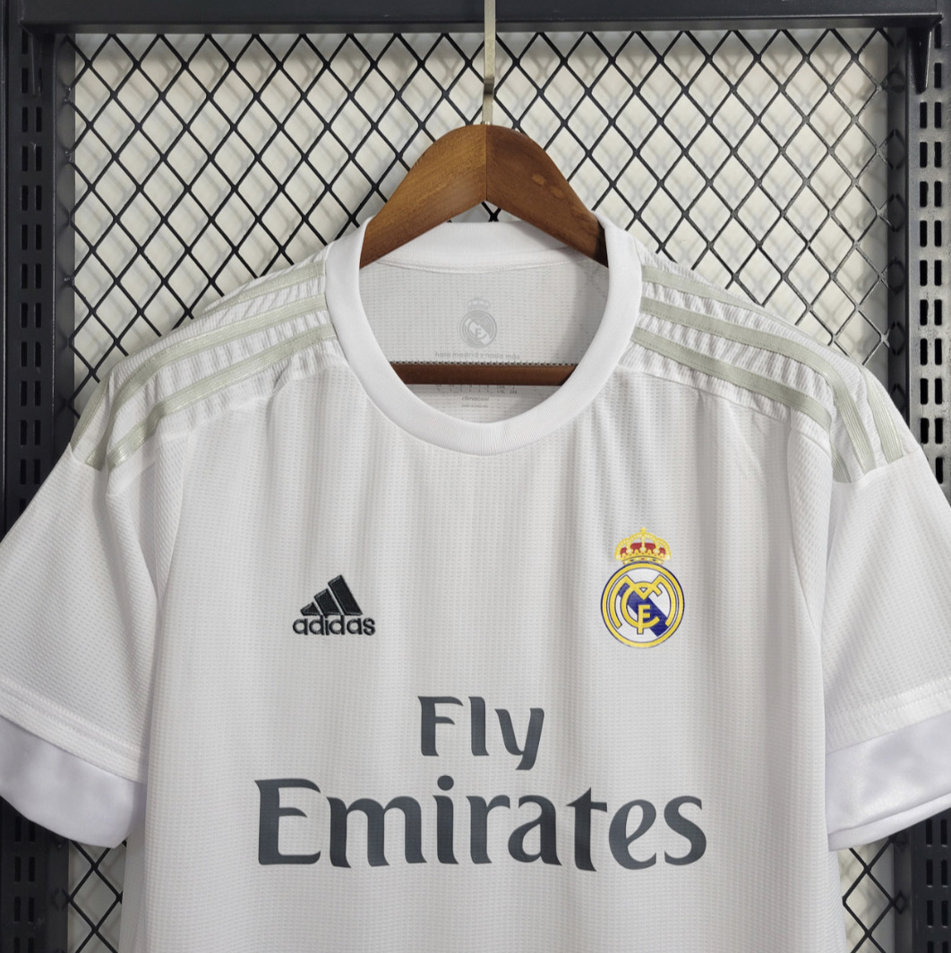 Real Madrid white football shirt chest close-up showing a round neckline, pale shoulder stripes, club crest and grey Fly Emirates lettering