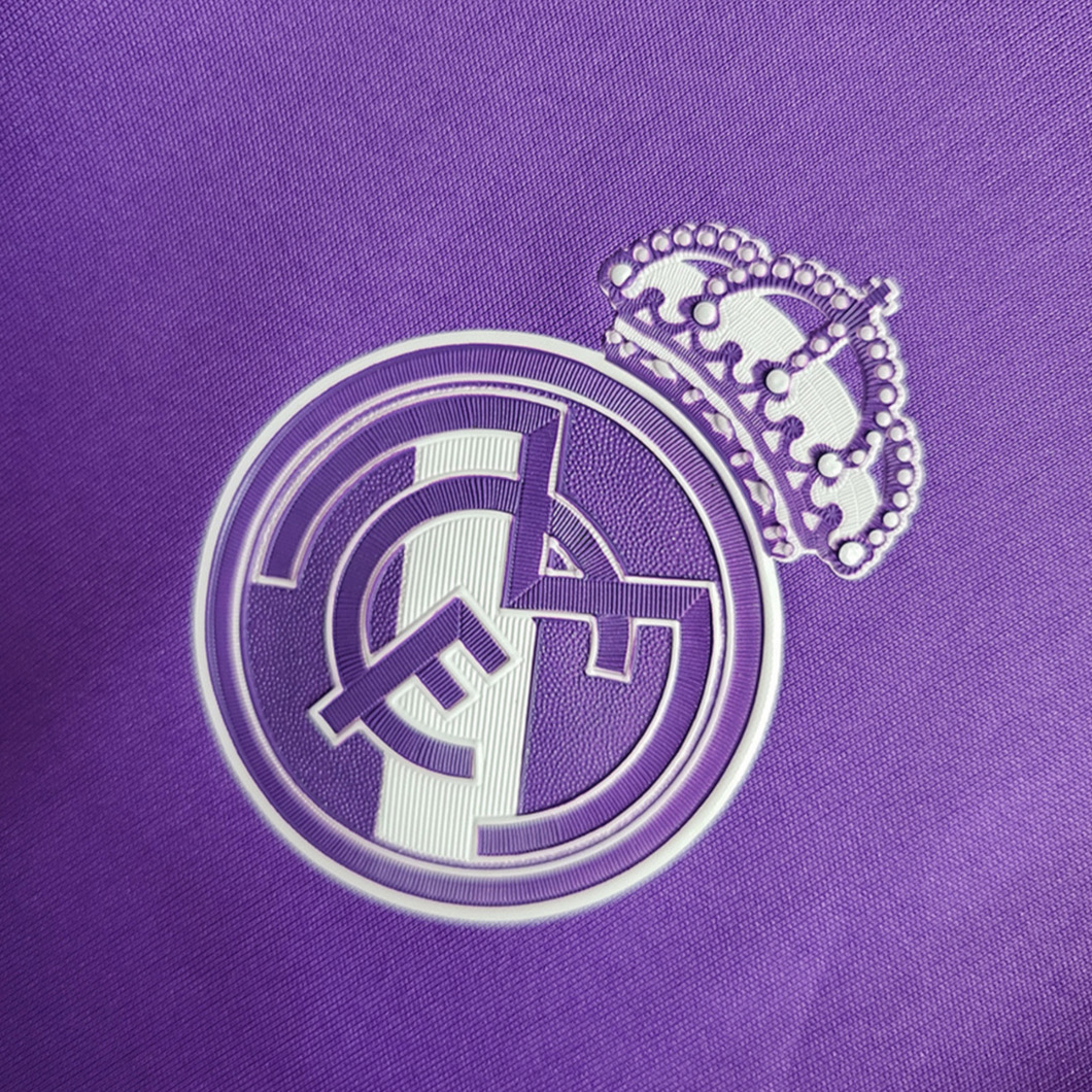 Real Madrid purple football shirt crest close-up showing a pale crowned club badge on purple fabric